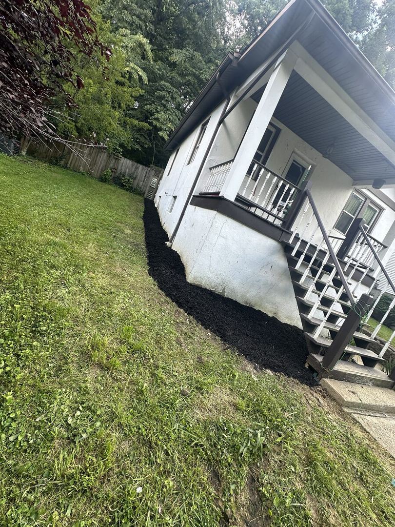 After: same side of the house with a fresh black mulch bed along the foundation and the grass cut