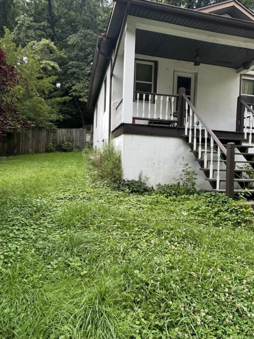 Before: side of a white house by the porch steps, with tall grass and weeds along the foundation