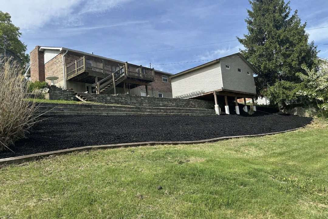 After: same slope cleared and covered in fresh black mulch along the wall, lawn cut